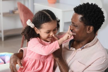 Mutlu Afro-Amerikalı adam ve küçük kızı evde oynuyorlar.