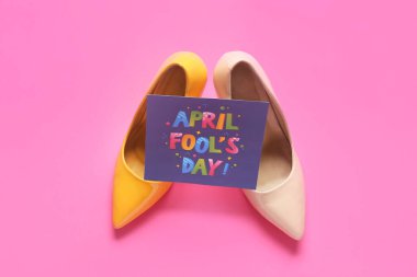 Pembe zemin üzerinde AYM FOOL GÜNÜ yazılı kadın ayakkabıları ve kart