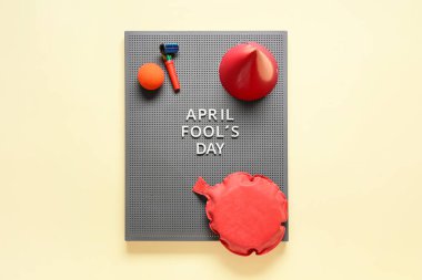 Gri tahta üzerinde APRIL FOOL 'S Day yazılı, osuruk yastığı ve sarı arka planda parti seti