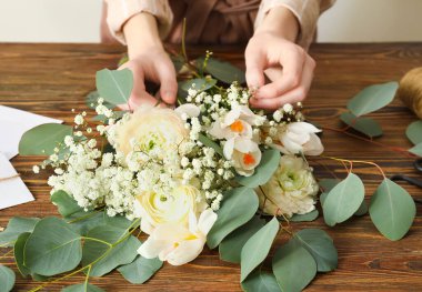 Kadın çiçekçi, ahşap masada güzel bir buket yapıyor, yakın plan.