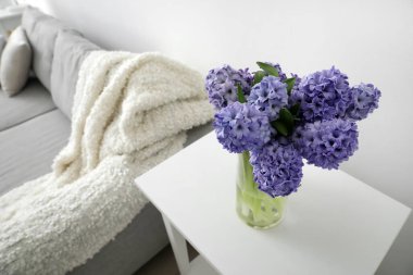 Oturma odasındaki ışık duvarının yanındaki masada sümbül çiçekli vazo.