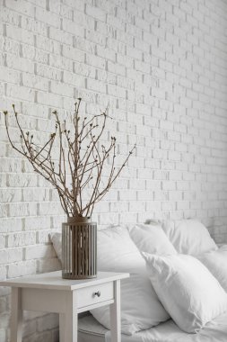 Beyaz tuğla duvarın yanındaki komodinin üzerinde ağaç dalları olan vazo.