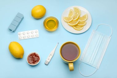 Çay, termometre, tıbbi maske, bal, limon, reçel ve mavi arka planda boğaz ağrısı için ilaç.