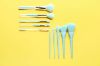 Sarı arkaplanda makyaj fırçaları, üst görünüm