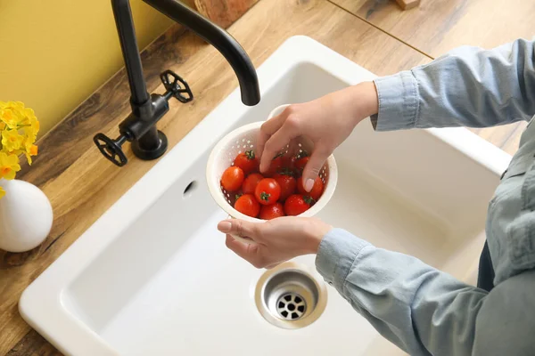 Woman washing cherry tomatoes in colander over sink, closeup
