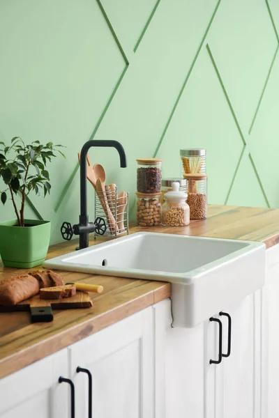 White sink with houseplant, food and kitchen utensils on counters near green wall
