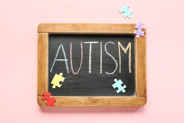 Pembe arka planda kelime AUTISM ve yapboz parçaları ile tebeşir tahtası