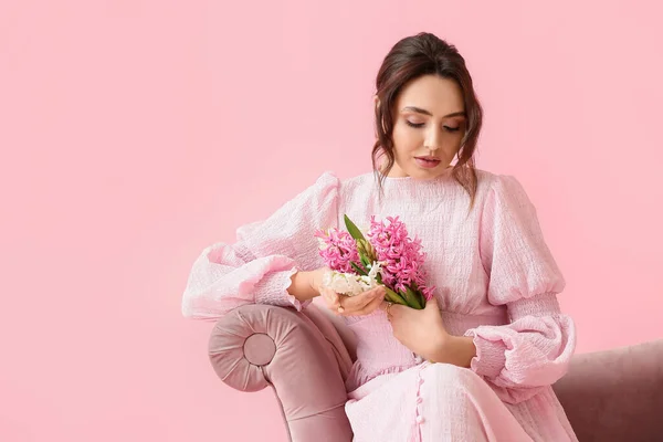 漂亮的年轻女子 开着百合花 坐在沙发上 粉色背景的衬托下 — 图库照片