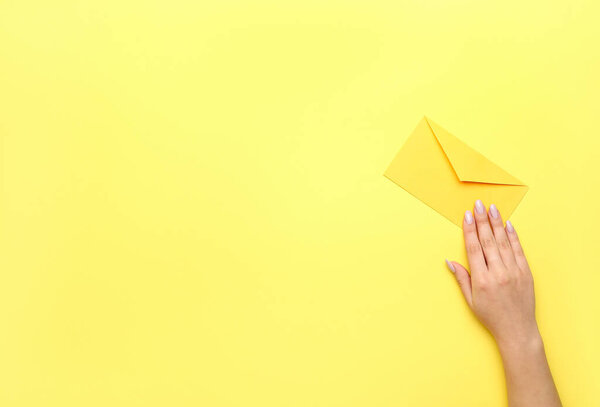 Female hand with beautiful manicure and envelope on yellow background