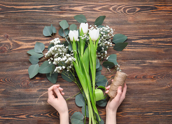 Female hands with bouquet of flowers and rope on wooden background