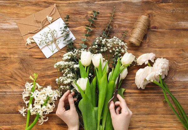 Female hands with beautiful spring flowers, scissors, rope and envelopes on wooden background
