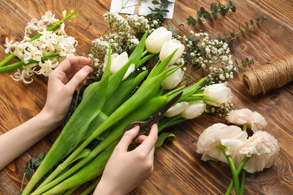 Female hands with beautiful spring flowers, scissors and rope on wooden background, closeup