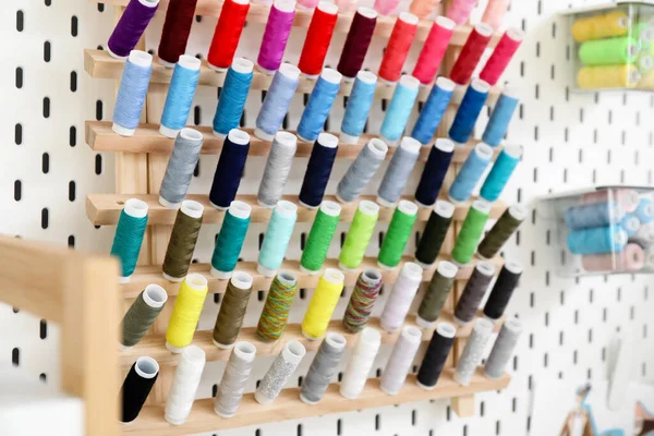 Stand with thread spools hanging on pegboard in atelier, closeup