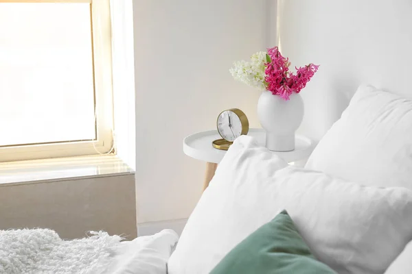 白い壁の近くのベッドサイドテーブルの上にヒヤシンスの花と目覚まし時計と花瓶 — ストック写真