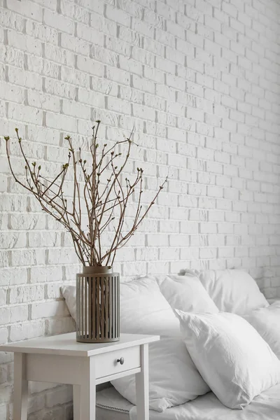Beyaz tuğla duvarın yanındaki komodinin üzerinde ağaç dalları olan vazo.