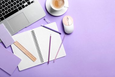 Boş defter, dizüstü bilgisayar, mor arka planda bir fincan kahve ve kırtasiye malzemesi.