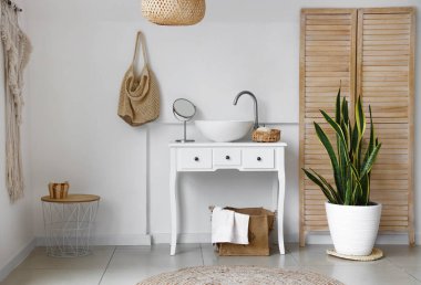 Lavabolu, çantalı ve çiçekli hafif banyonun içi.