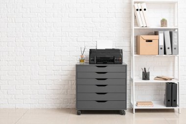 Çağdaş yazıcı ve raf ünitesi olan çekmeceler beyaz tuğla duvarın yanında.