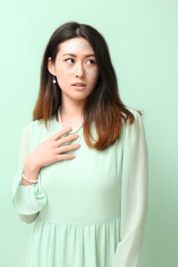 Parlak makyajlı genç Asyalı kadın renk arkaplanda kolyeye dokunuyor