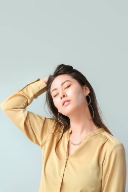 Parlak makyajlı ve kapalı gözlü Asyalı bir kadın açık arkaplanda saçlarına dokunuyor.