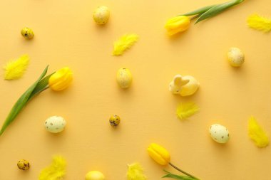 Sarı arka planda boyanmış Paskalya yumurtaları, tavşanlar ve lale çiçekleri.