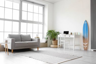 Rahat bir kanepe, iş yeri ve iç aydınlık odada sörf tahtası.