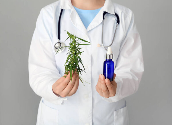 Женщина-врач с бутылкой конопляного масла на сером фоне, крупным планом