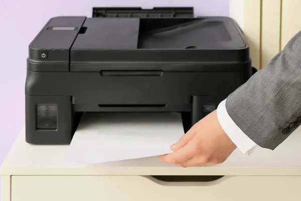 Businesswoman printing document on chest of drawers near color wall, closeup