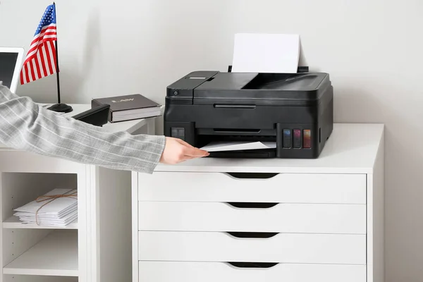 Businesswoman printing document near light wall in office