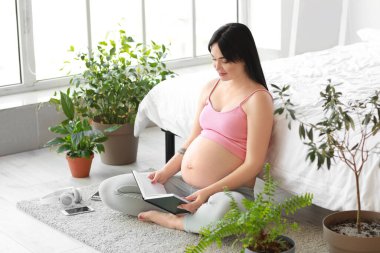 Genç hamile kadın yatak odasında kitap okumak