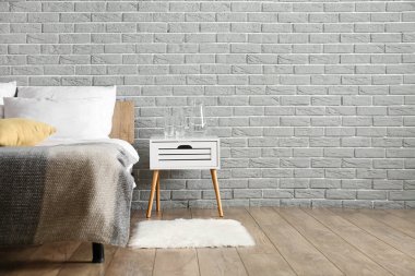 Yatak odasındaki gri tuğla duvarın yanında su ve bardaklı sürahi.