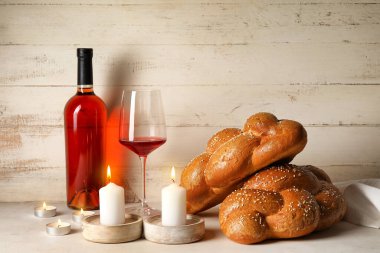 Şarap ve beyaz ahşap arka planda parlayan mumlarla geleneksel challah ekmeği. Şabat Şalom