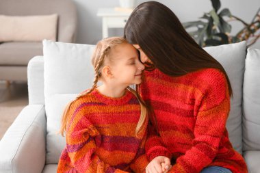 Küçük kız ve annesi sıcak kazaklar içinde evdeki kanepede oturuyorlar.