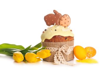 Kurabiyelerle süslenmiş lezzetli Paskalya pastası, beyaz arka planda boyanmış yumurta ve lale çiçekleri.