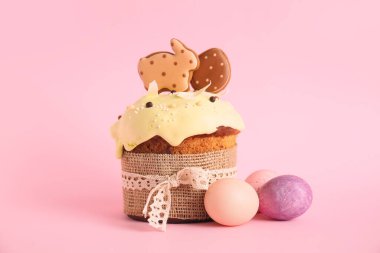Kurabiyelerle süslenmiş lezzetli Paskalya pastası ve pembe arka planda boyanmış yumurtalar.