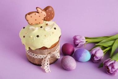 Kurabiye, çiçek ve mor arka planda boyanmış yumurtalarla süslenmiş lezzetli Paskalya pastası.