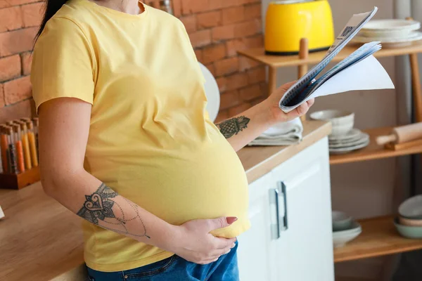 Молодая Беременная Женщина Читает Газеты Кухне — стоковое фото
