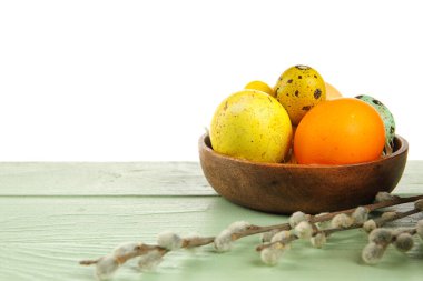 Bowl with painted Easter eggs and pussy willow on table against white background
