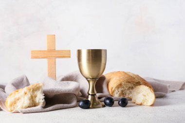 Ekmekli bir bardak şarap ve arka planda haç.