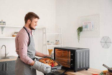 Genç adam, mutfaktaki fırına lezzetli yiyeceklerle birlikte fırın koyuyor.