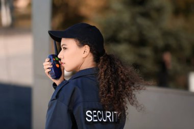 Dışarıdaki binanın yakınında radyo vericisi olan Afro-Amerikalı bir kadın güvenlik görevlisi.