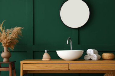 Banyoda yeşil duvarın yanında lavabo, sabun ve havlu olan masa.