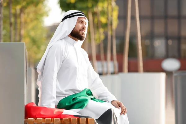 一位英俊的穆斯林男子 高举阿联酋国旗 坐在室外长椅上 — 图库照片