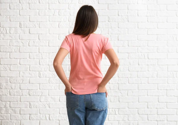 stock image Young woman in blank t-shirt on white brick background, back view