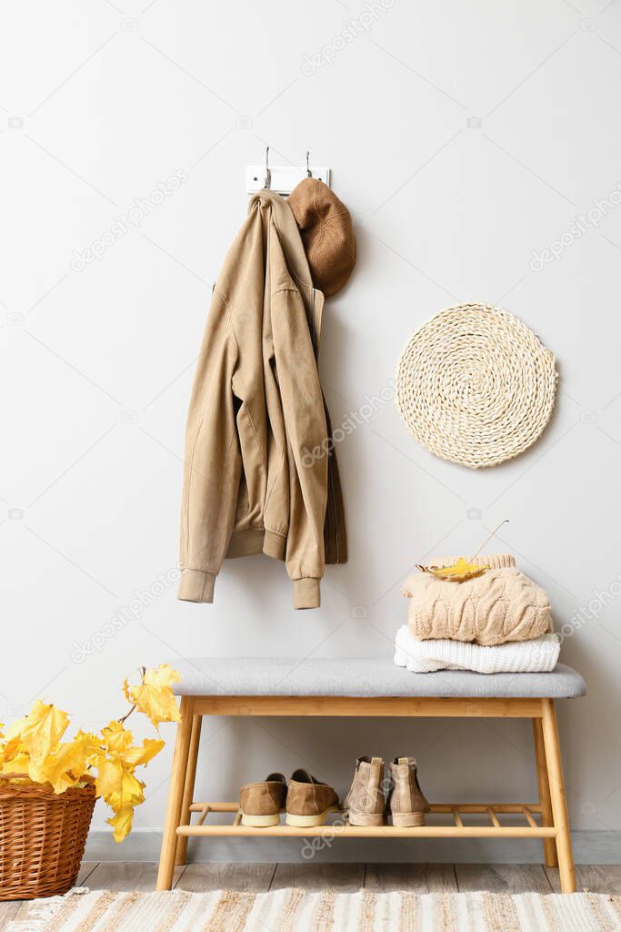 Jacket and hat hanging on light wall in stylish hallway