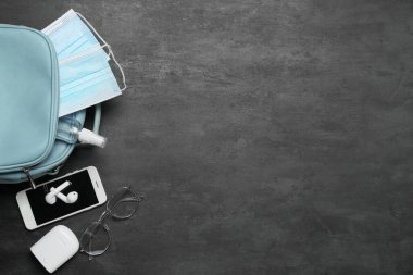 Tıbbi maskeli çanta, cep telefonu ve siyah arka planda kulaklık.