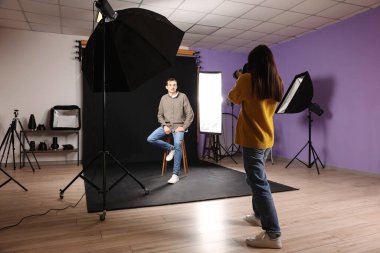 Fotoğraf stüdyosunda genç bir adamın fotoğrafını çeken kadın fotoğrafçı.