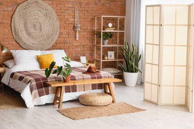 Şık bir yatak odası, katlanır ekran ve ahşap bir bank.