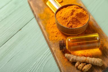 Bir şişe yağ, zerdeçal kökü ve yeşil ahşap arka planda toz bulunan kase.