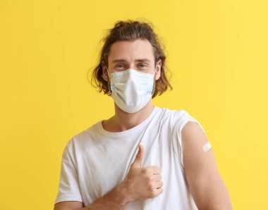 Aşıdan sonra maske takan genç adam renk arkaplanında başparmağını gösteriyor.